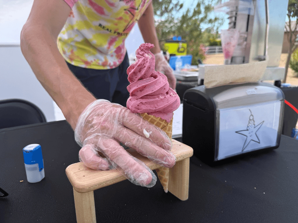 Pink real-fruit soft-serve in a waffle cone at a farmers market stand